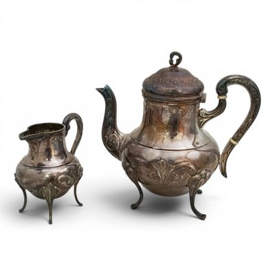 two silver teapots and a cup on a stand on a white background