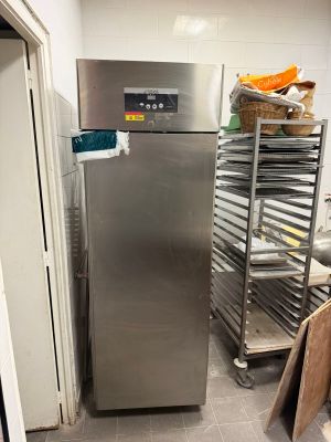 a stainless steel refrigerator in a kitchen next to a rack of food