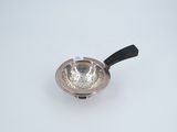a small silver bowl with a black handle on a white surface