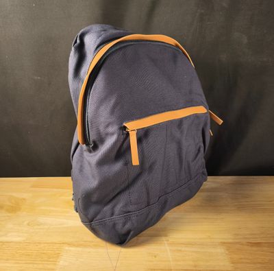 un sac à dos gris et orange posé sur une table en bois, avec un mur noir en arrière-plan