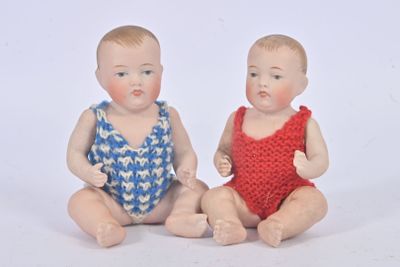 two baby dolls sitting next to each other on a white surface