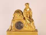 a gold clock with a woman sitting on top of it