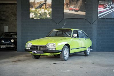 une voiture verte garée dans un garage, près d'un mur orné de tableaux