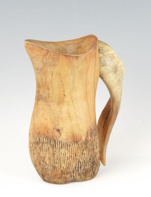 une cruche en bois avec une anse recourbée, posée sur une surface blanche