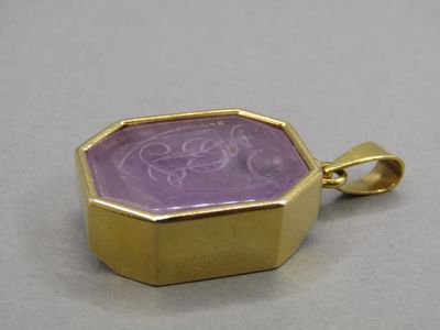 une image représentant un pendentif en pierre dorée et violette posé sur une surface blanche