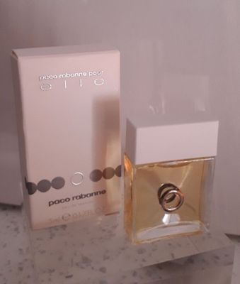 un flacon de parfum et son coffret posés sur un plan de travail, près d'un mur blanc