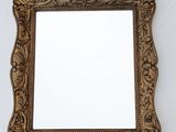 un miroir au cadre doré ouvragé accroché à un mur blanc, sur fond blanc