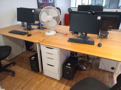 un bureau sur lequel sont posés deux écrans d'ordinateur et un ventilateur