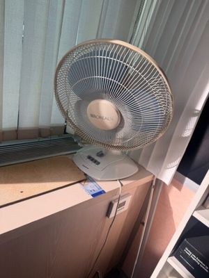 un ventilateur posé sur un bureau près d'une fenêtre