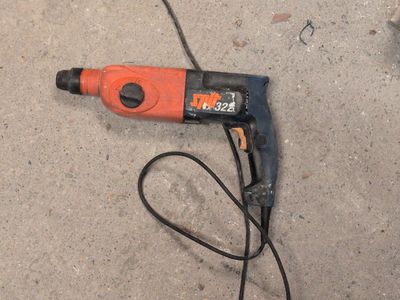 an orange and black electric drill sitting on the ground next to a black cord
