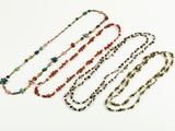 three long necklaces with multi colored beads on a white surface
