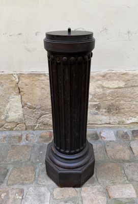 une poubelle noire posée sur un trottoir pavé