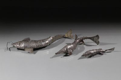 plusieurs poissons en métal posés sur une surface blanche avec un fond noir