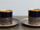 une paire de tasses et soucoupes plaquées argent posées sur une table