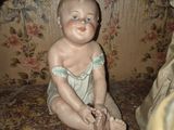 a baby doll sitting on the floor next to a vase