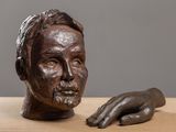 sculpture représentant la main d'un homme posée sur une table, à côté d'un buste d'homme