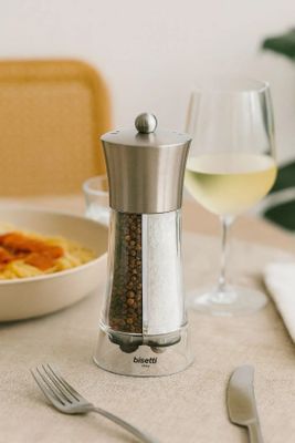 un moulin à poivre en argent et un verre de vin posés sur une table