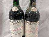 two bottles of red wine sitting next to each other on a white surface