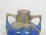 un vase bleu à deux anses posé sur une surface blanche