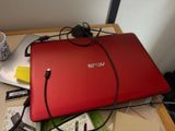 un ordinateur portable rouge posé sur un bureau, avec son chargeur