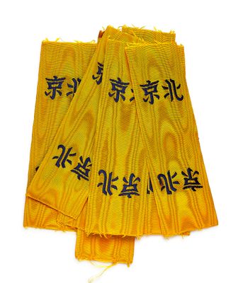 trois morceaux de tissu jaune portant des inscriptions en chinois, posés sur une surface blanche