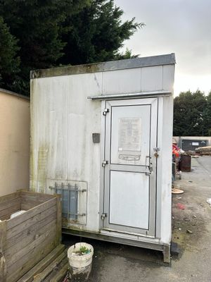 a white toilet sitting outside of a building next to a trash can