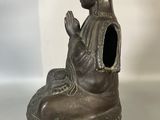 bronze statue of a woman sitting on a rock with her hands clasped
