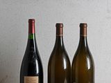 three bottles of wine sit on a wooden table next to a bottle of wine