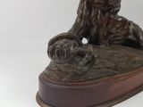 bronze statue of a lion on a wooden base with a ball in its mouth