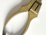 une petite pince en laiton posée sur une surface blanche