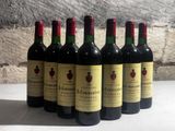 six bouteilles de vin rouge alignées sur une table devant un mur de pierre