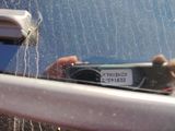 reflection of a person holding a camera in the rear window of a car