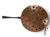 an old copper frying pan with holes and a handle