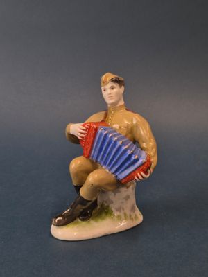 une figurine représentant un homme assis sur un rocher, un accordéon à la main