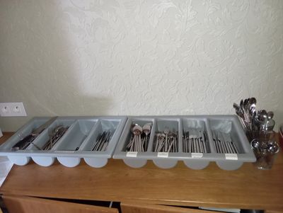 several trays of utensils are lined up on a wooden table