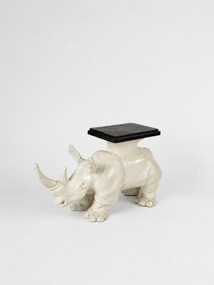 une statue de rhinocéros blanc coiffé d'un chapeau noir, assis sur une surface blanche