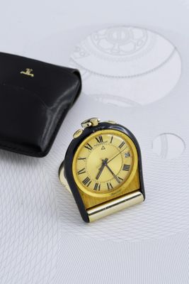 une petite horloge posée à côté d'un portefeuille sur une table