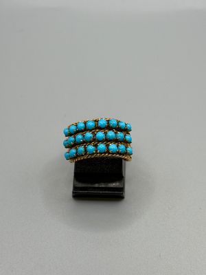 un gros plan d'une bague en or et turquoise posée sur un socle noir