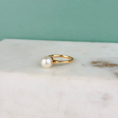 un gros plan d'une bague en or ornée d'une perle, posée sur un bloc de marbre