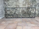 a black iron fence on a brick floor with a stone wall in the background