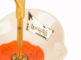 a gold spoon in a white bowl with a red liquid in it