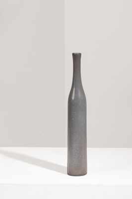 un vase gris posé sur une surface blanche, avec l'ombre d'une personne
