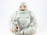 une statue représentant un Bouddha souriant, assis sur une surface blanche