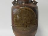 un vase marron avec un couvercle marron posé sur une surface blanche