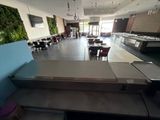 many tables and chairs in a restaurant with a wall of plants behind them