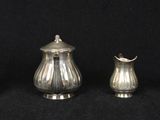 three silverplated teapots and a sugar shaker on a black background