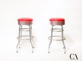 une paire de tabourets chromés avec des assises rembourrées rouges sur fond blanc