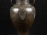 un vase antique en bronze muni d'anses, sur fond noir