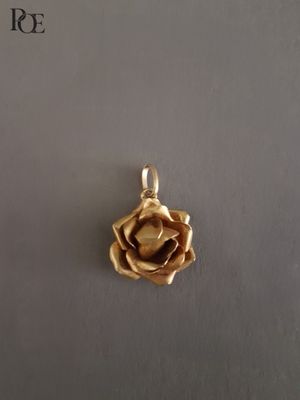 un gros plan d'un pendentif en forme de rose dorée posé sur une surface blanche