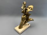 une statue en bronze représentant un homme tenant un livre, posée sur un socle en bois